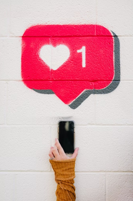 Hand holding a smartphone next to a like drawing on a white wall